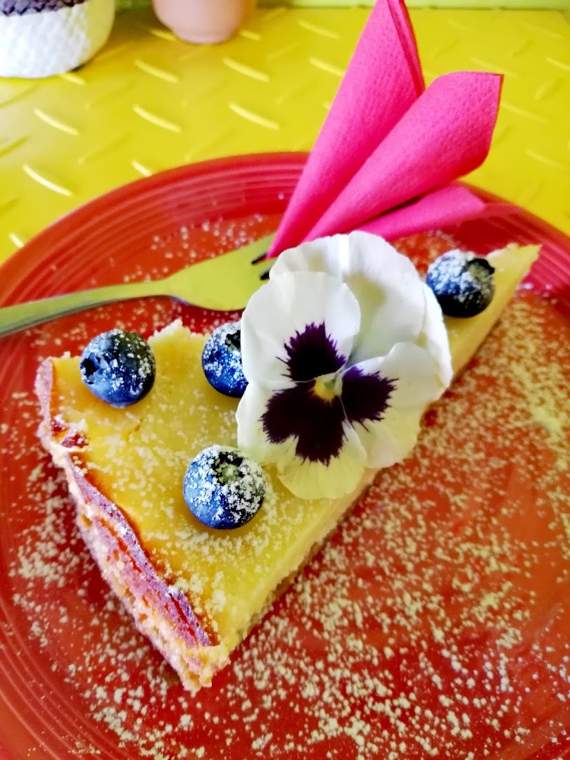 A slice of lemon tart with blueberries and an edible pansy on a red plate