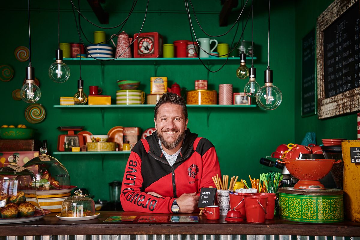 Gideon Swart smiling behind the café counter beneath hanging festoon bulbs
