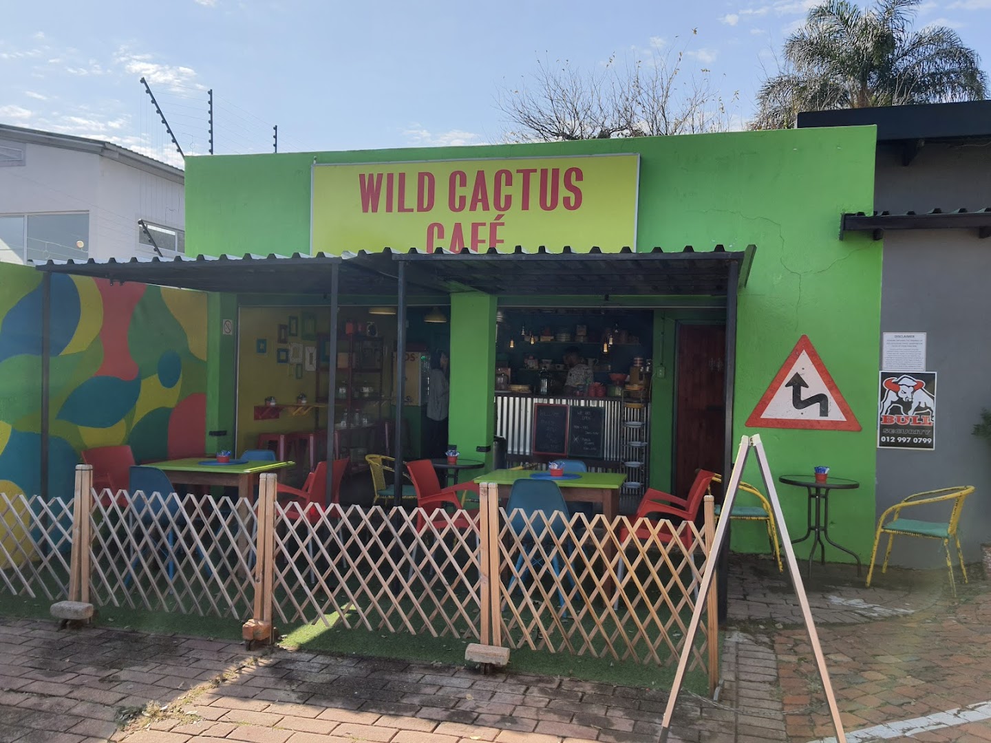 The early Wild Cactus Café storefront painted bright green, with colourful tables on the pavement